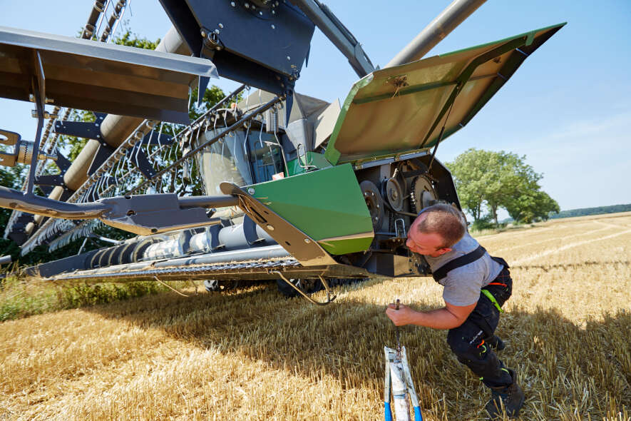 Servicetechniker prüft Schneidwerk eines Fendt Mähdreschers während der Weizenernte auf dem Feld.