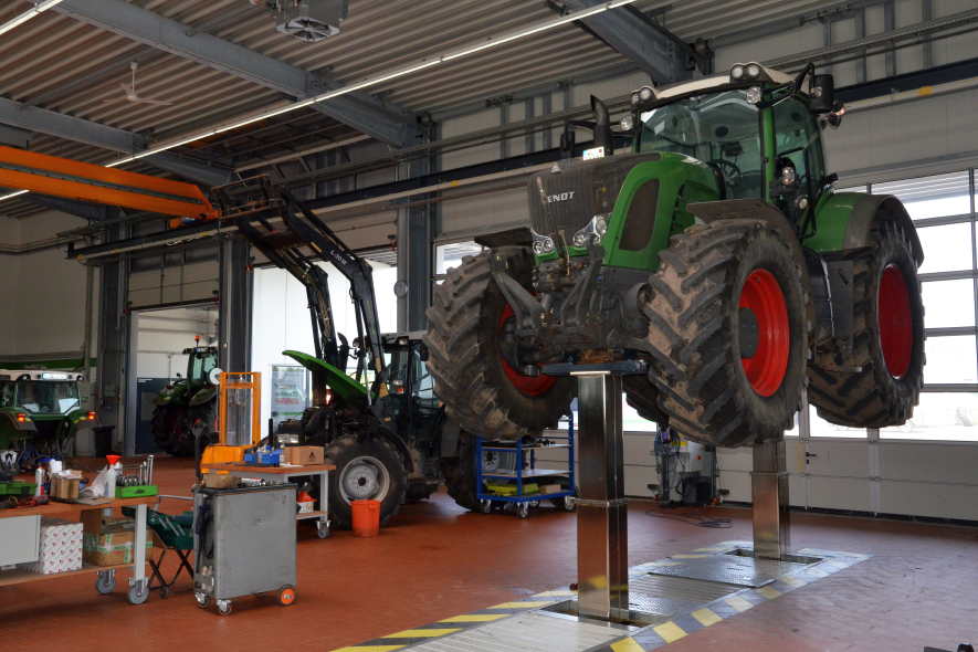 Mechaniker bei Reparatur unter Traktor auf Hebebühne in der Werkstatt