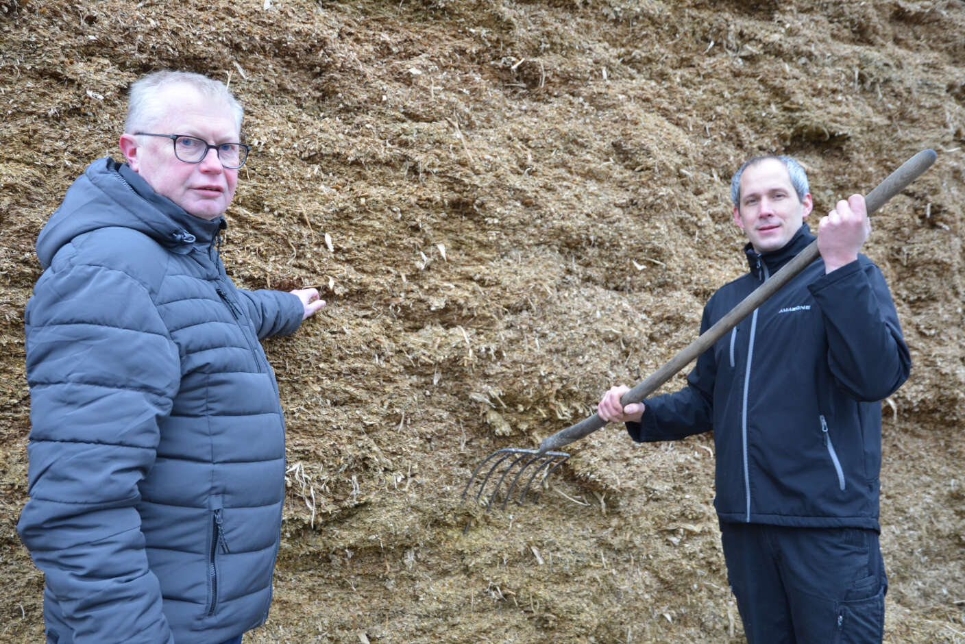 Zwei Herren, einer davon mit einer Mistgabel in der Hand, stehen neben Silage.
