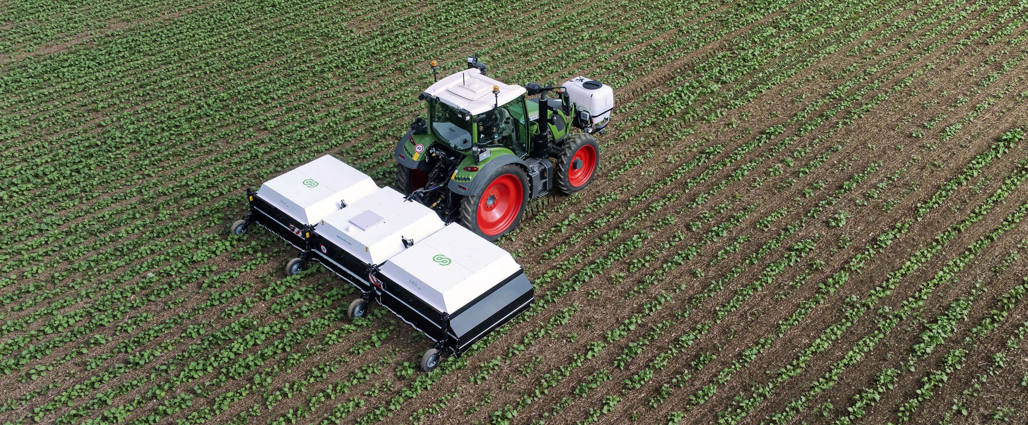 Eine ARA Feldspritze an einem Fendt Traktor fährt über ein Feld und wird von einer Drohne aufgenommen.