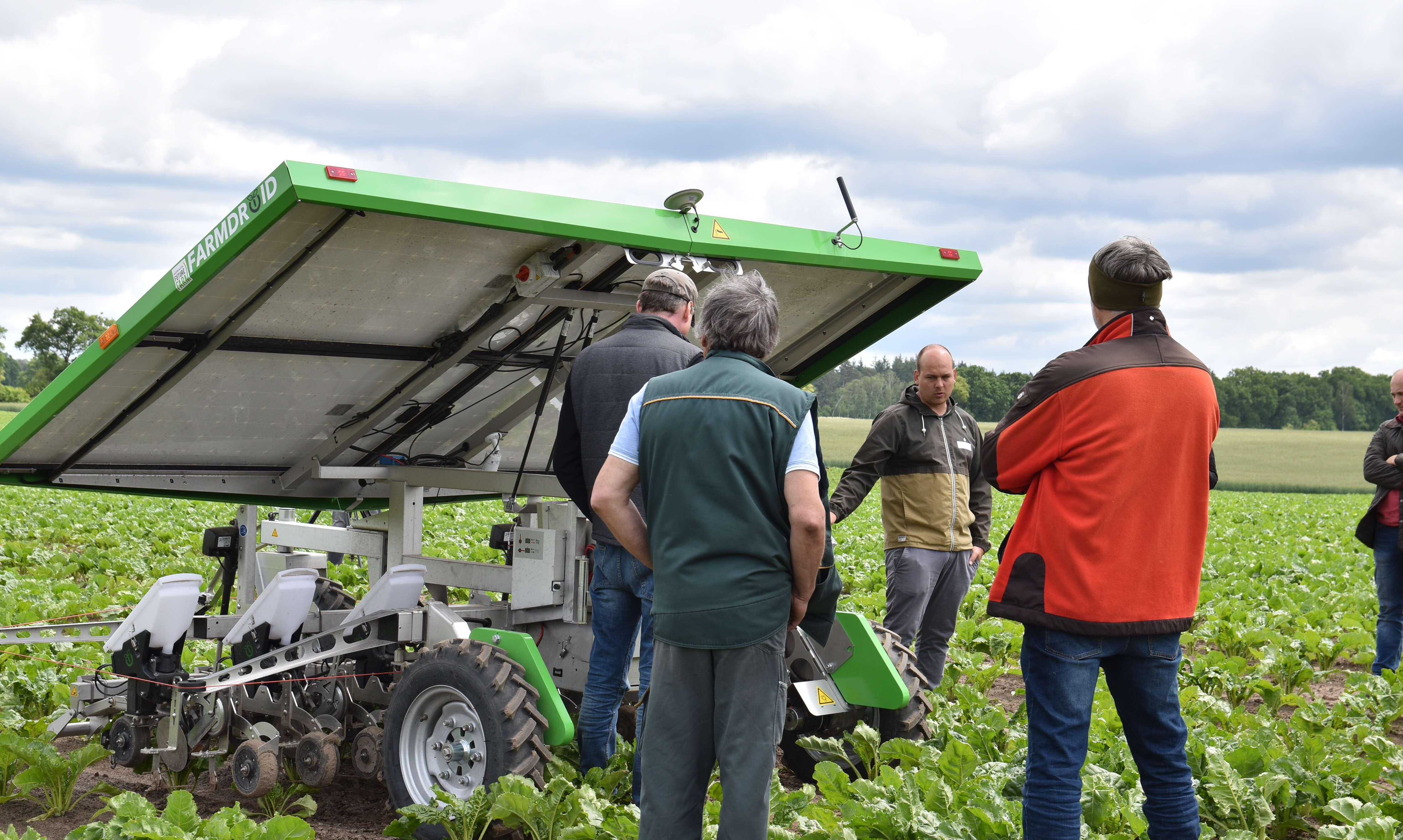 Der Feldroboter Farmdroid FD20 steht auf einem Acker, ringsherum stehen mehrere Personen. 