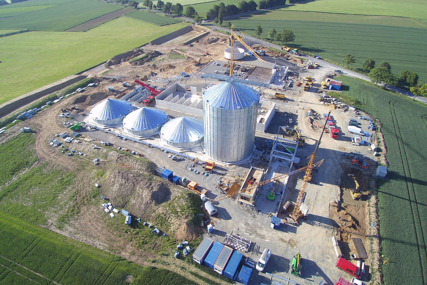 Rundsilo aus stahl welches in der Sonne glänzt. Um das Silo herum befindet sich eine Baustelle.