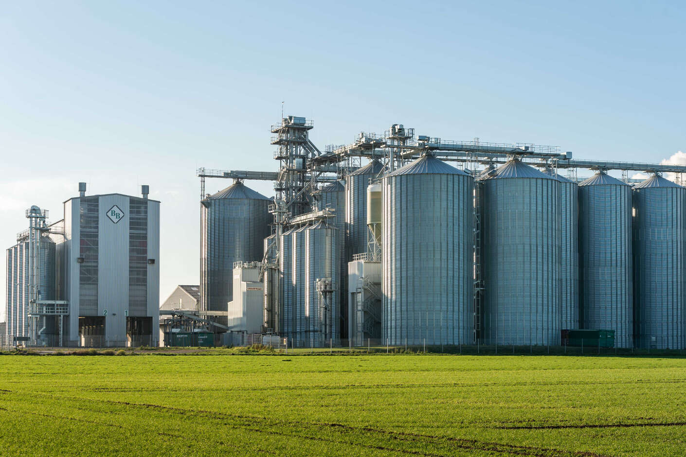 Mehrere Stahlsilos stehen nebeneinander vor einer grünen Wiese. Links neben den Silos befindet sich ein Annahmegebäude.