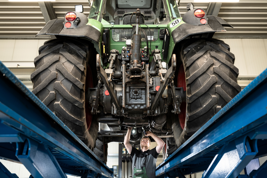 Mechaniker bei Reparatur unter Traktor auf Hebebühne in der Werkstatt
