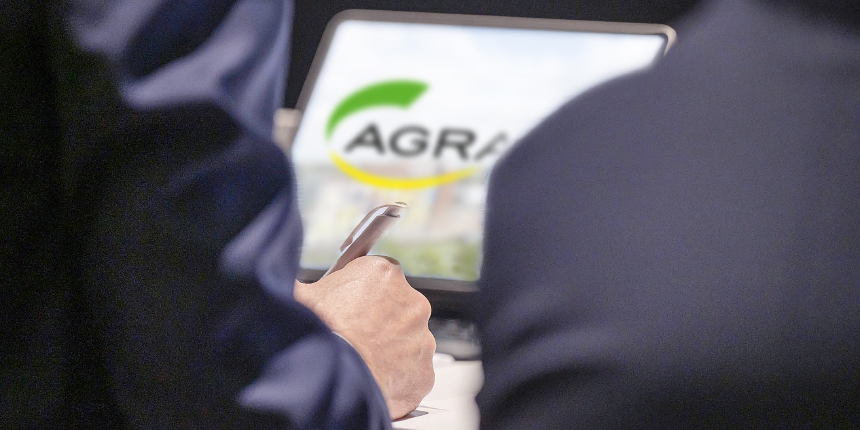 Blick von hinten: Zwei Personen im Anzug sitzen nebeneinander - AGRAVIS-Logo auf Laptop in der Mitte