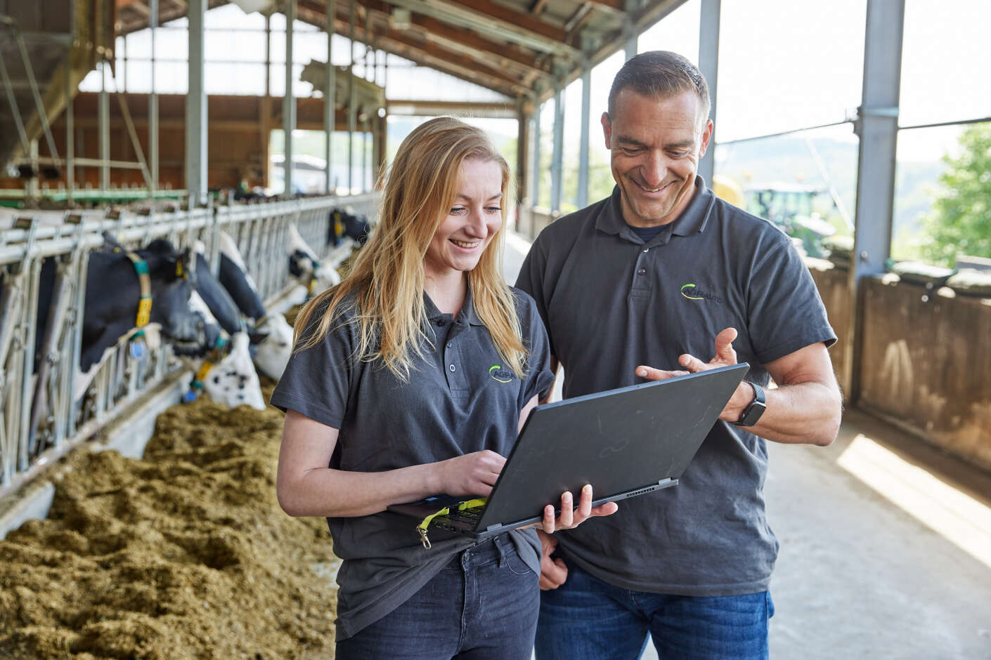 Berater vor Futtertisch im Rinderstall mit Laptop in der Hand