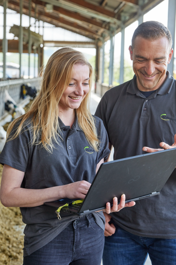 Berater vor Futtertisch im Rinderstall mit Laptop in der Hand