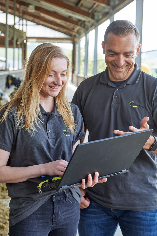 Berater vor Futtertisch im Rinderstall mit Laptop in der Hand