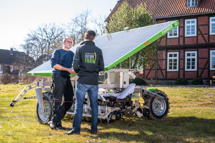 Zwei Mitarbeiter am Farmdroid FD20 auf einer Wiese vor dem Schulungsgebäude der Future Farm