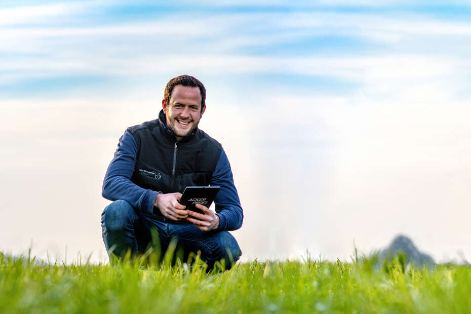 Mann mit Tablet in der Hand hockt auf Grasfläche