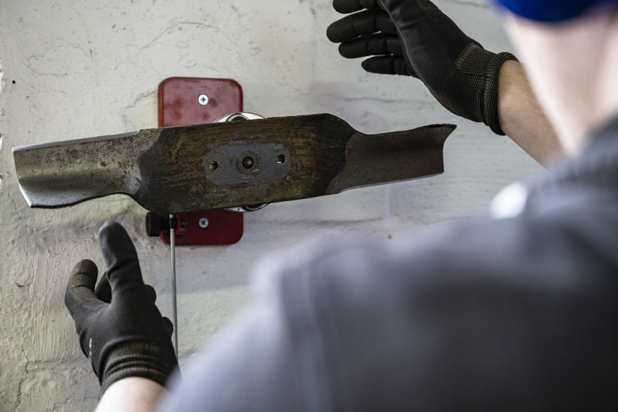 Mähmesser wird von Werkstattmitarbeiter auf Halterung zur Bearbeitung gesetzt