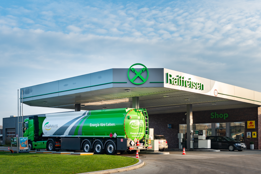 Tankstelle wo ein AGRAVIS LKW tankt. Das Tankstellendach ist hellgrau mit grüner Raiffeisen-Schrift und grünem Giebelkreuz.