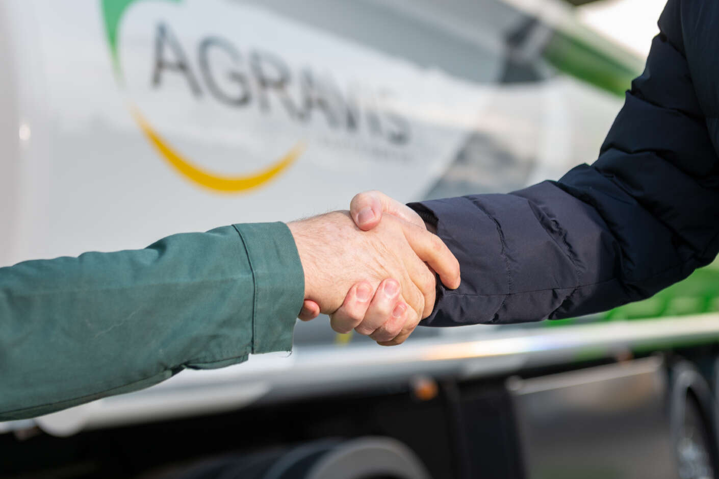Ein Handschlag von zwei Personen. Im Hintergrund ist ein Tankwagen mit Agravis Logo.