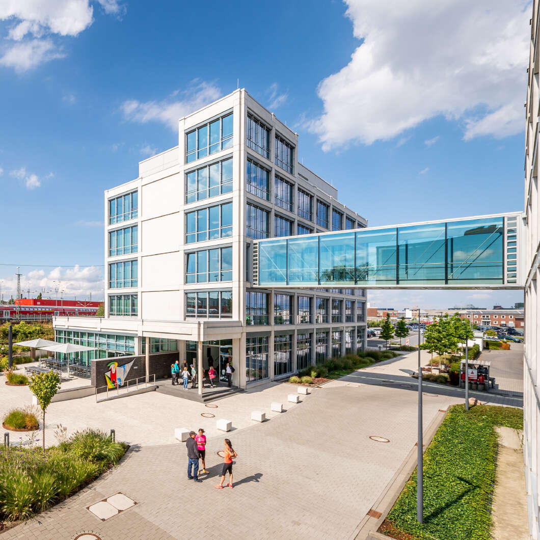 Sechsstöckiges Gebäude mit Betonfertigteiloptik mit großen Fenstern und einem großen Eingangsbereich. 