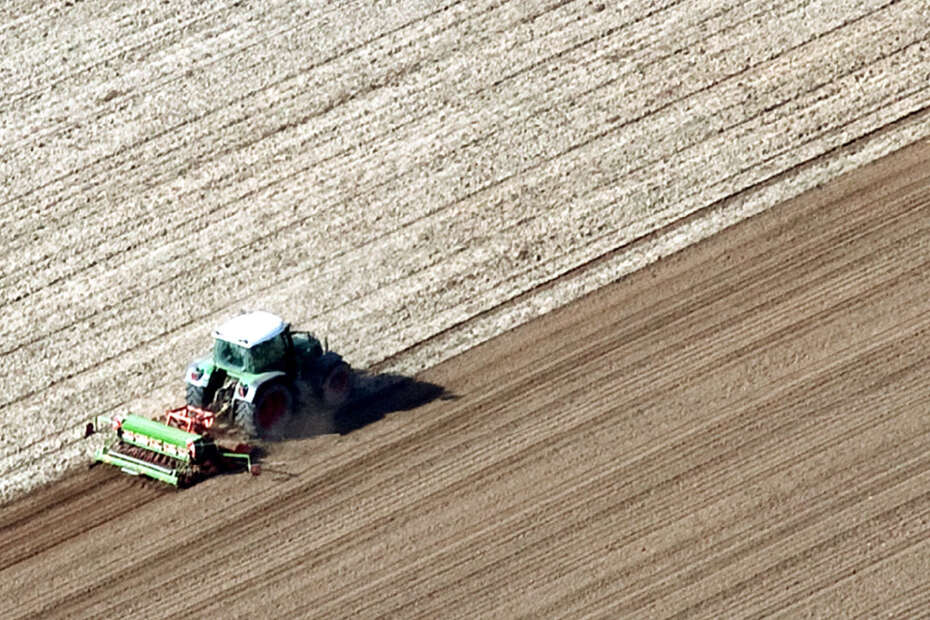Ein Schlepper fährt über ein gepflügtes Feld und drillt Saatgut aus.