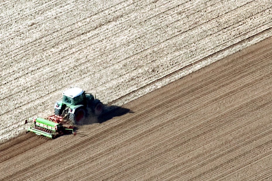 Ein Schlepper fährt über ein gepflügtes Feld und drillt Saatgut aus.