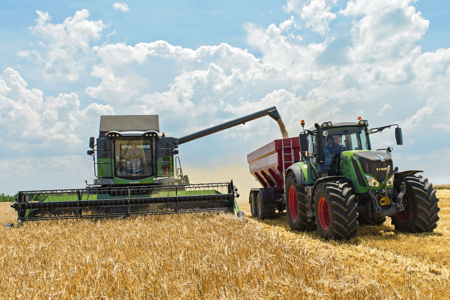 Mähdrescher entleert Ernte in Anhänger, Traktor daneben auf Getreidefeld