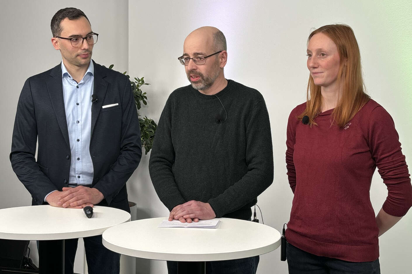 Drei Referenten der Veranstaltung Grünland Virtuell stehen nebeneinander an Tischen.