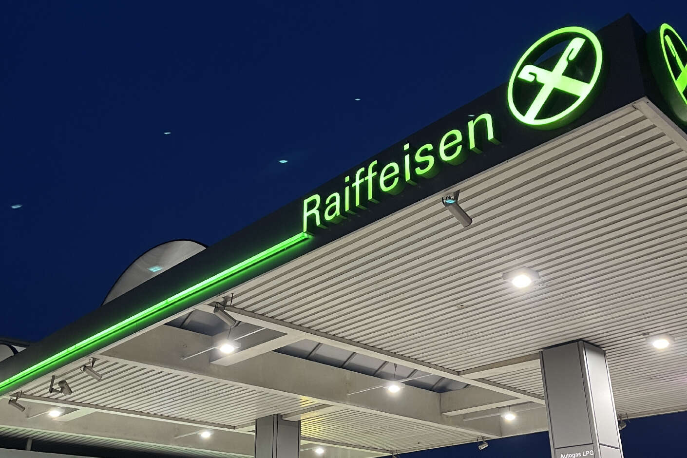 Raiffeisen Tankstelle bei Nacht. Das Giebelkreuz ist beleuchtet.