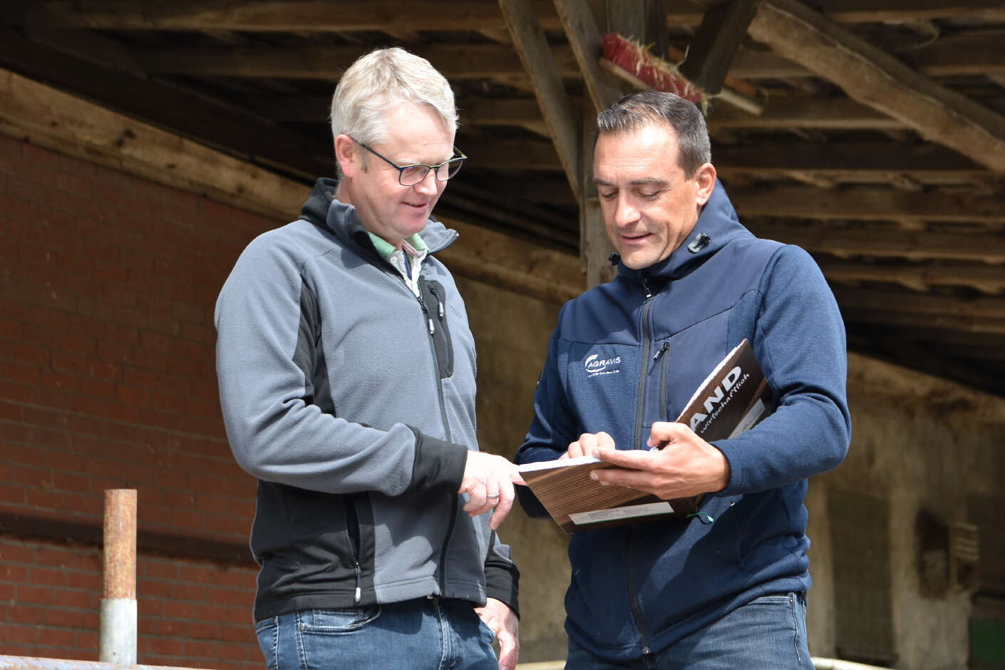 Frank Heise und Dirk Rehbock steen mit einer Mappe in der Hand im Kuhstall.