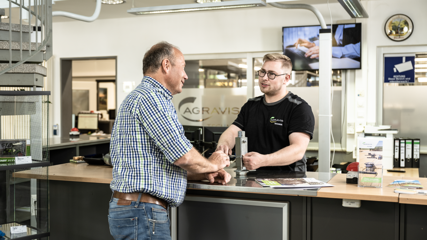 Customer consultation at AGRAVIS Technik counter with spare part in hand