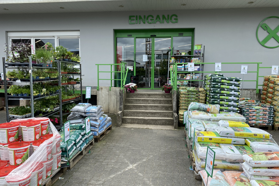 Eingang zum Raiffeisen Markt Grevenbrück Lennestadt mit Blumeerde & Dünger im Vordergrund