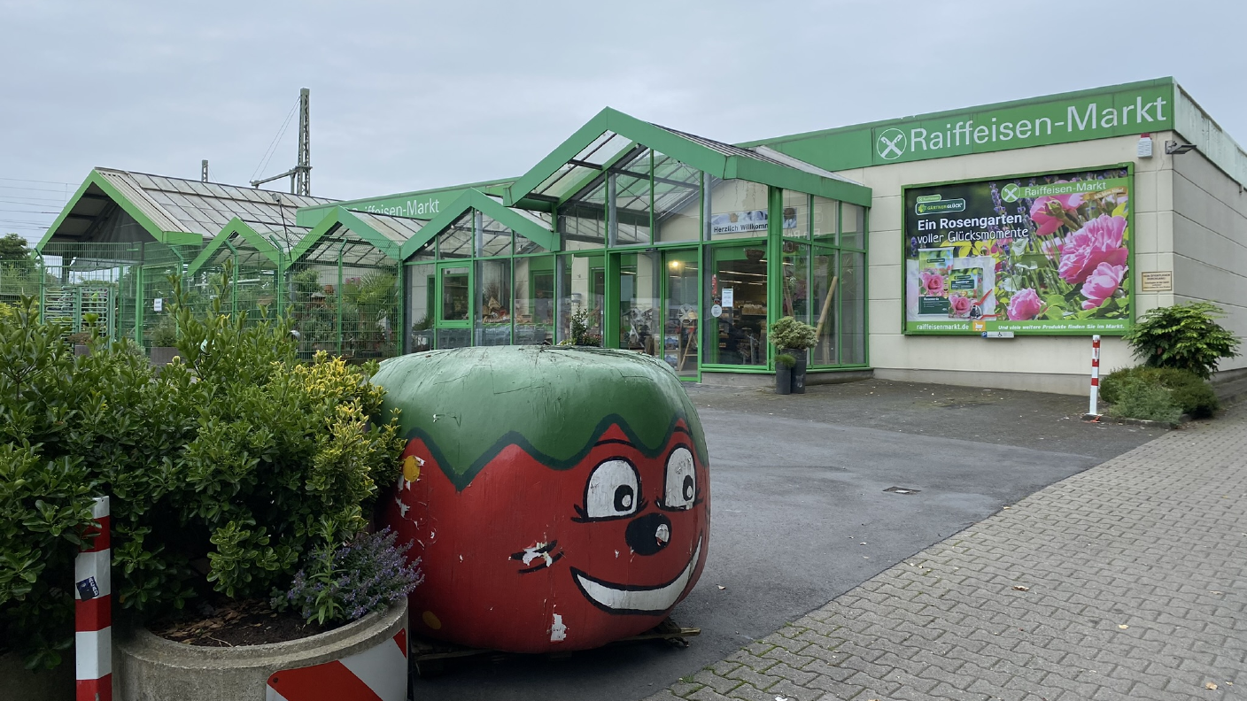 Eingang zum Raiffeisen-Markt im Vordergrund Rundballen in Erdbeerfolie