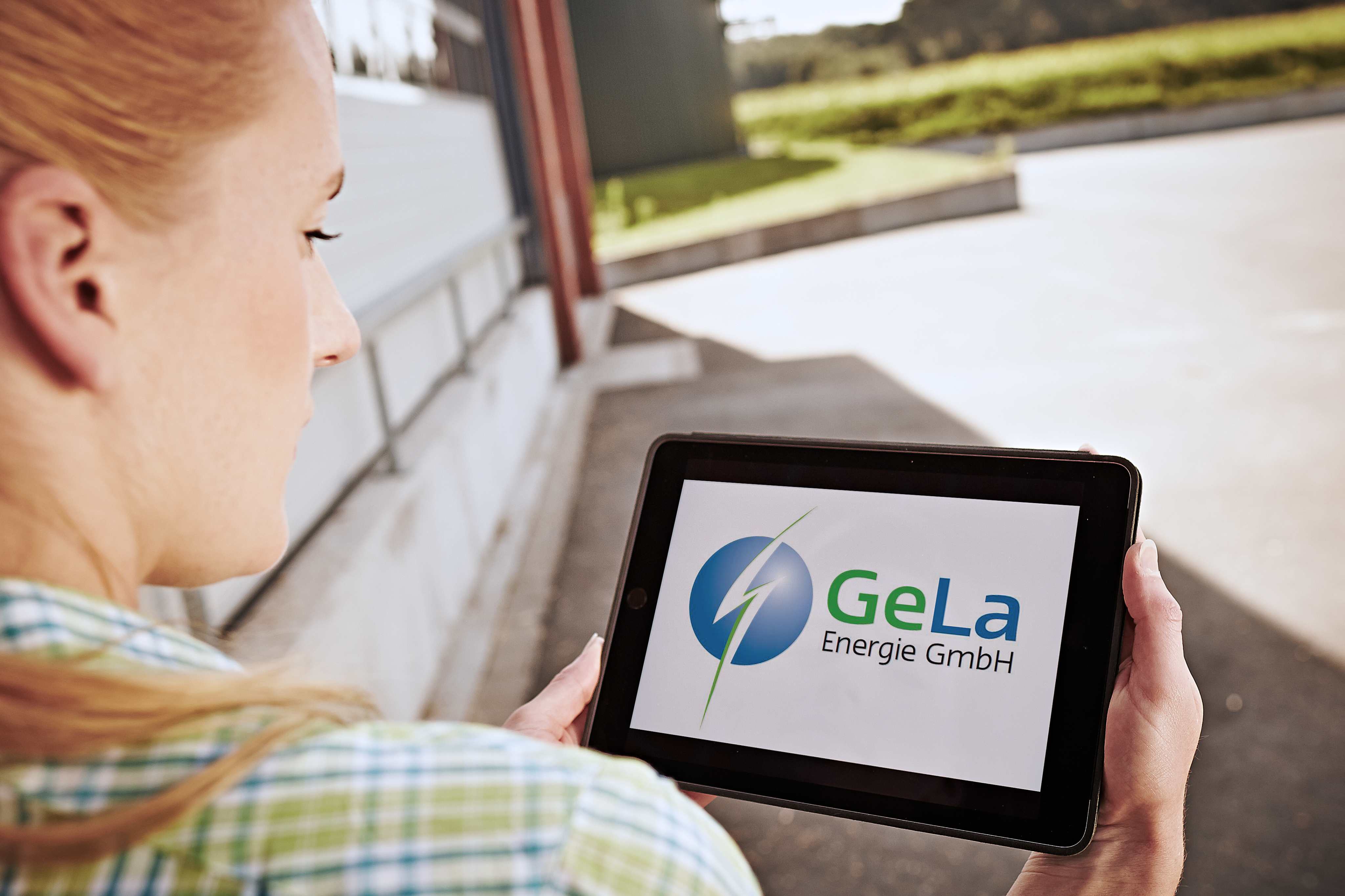 Eine Frau schaut aufs ein Tablet. Auf dem tablet ist das Logo der Gela zu sehen. 