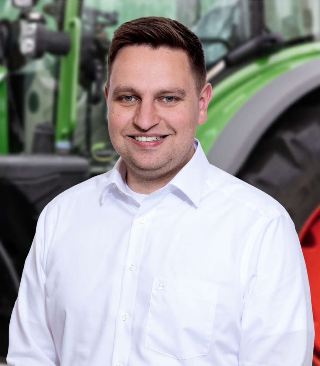 Thomas Döring in Fröndenberg lächelt in die Kamera. Ein Fendt Traktor steht im Hintergrund.   