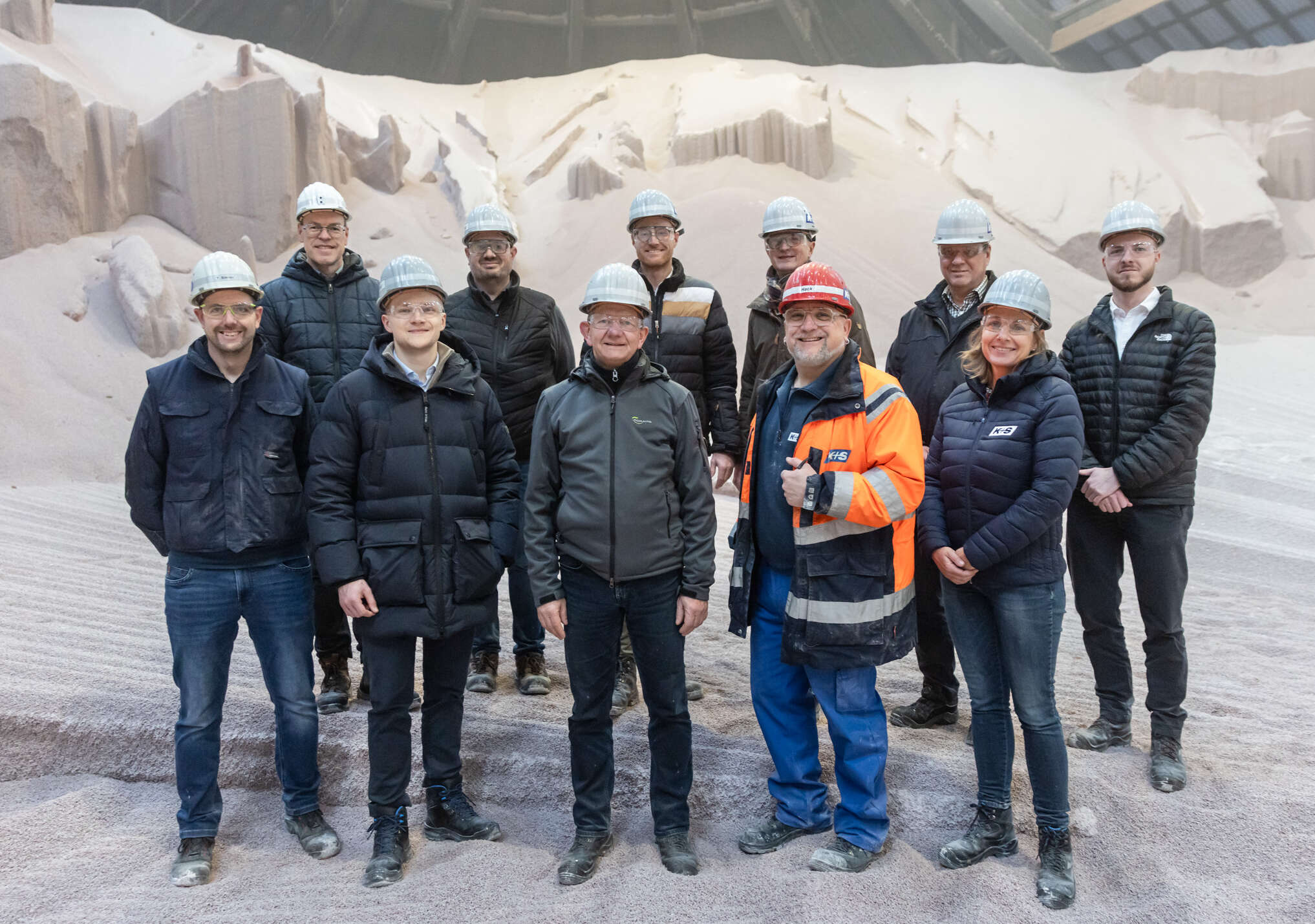 Elf Personen stehen in einer hellen Halle vor einem Berg mit weißem Dünger