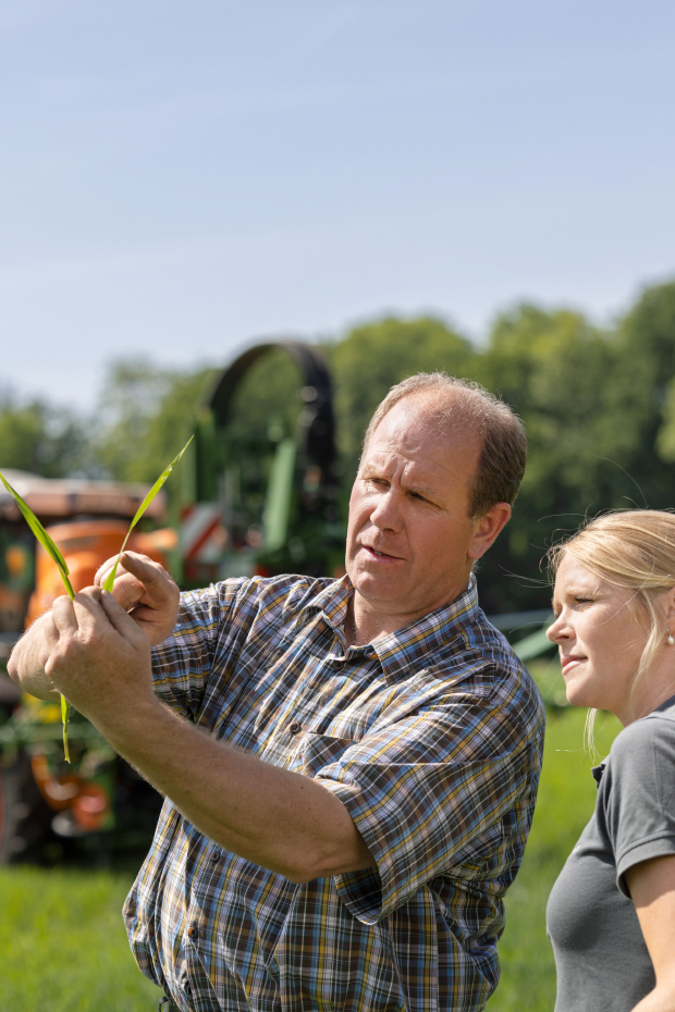Landwirt und AGRAVIS-Mitarbeiterin begutachten Pflanze - Düngetechnik im Hintergrund
