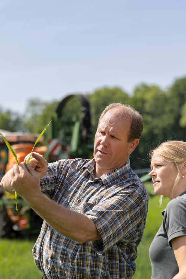 Landwirt und AGRAVIS-Mitarbeiterin begutachten Pflanze - Düngetechnik im Hintergrund