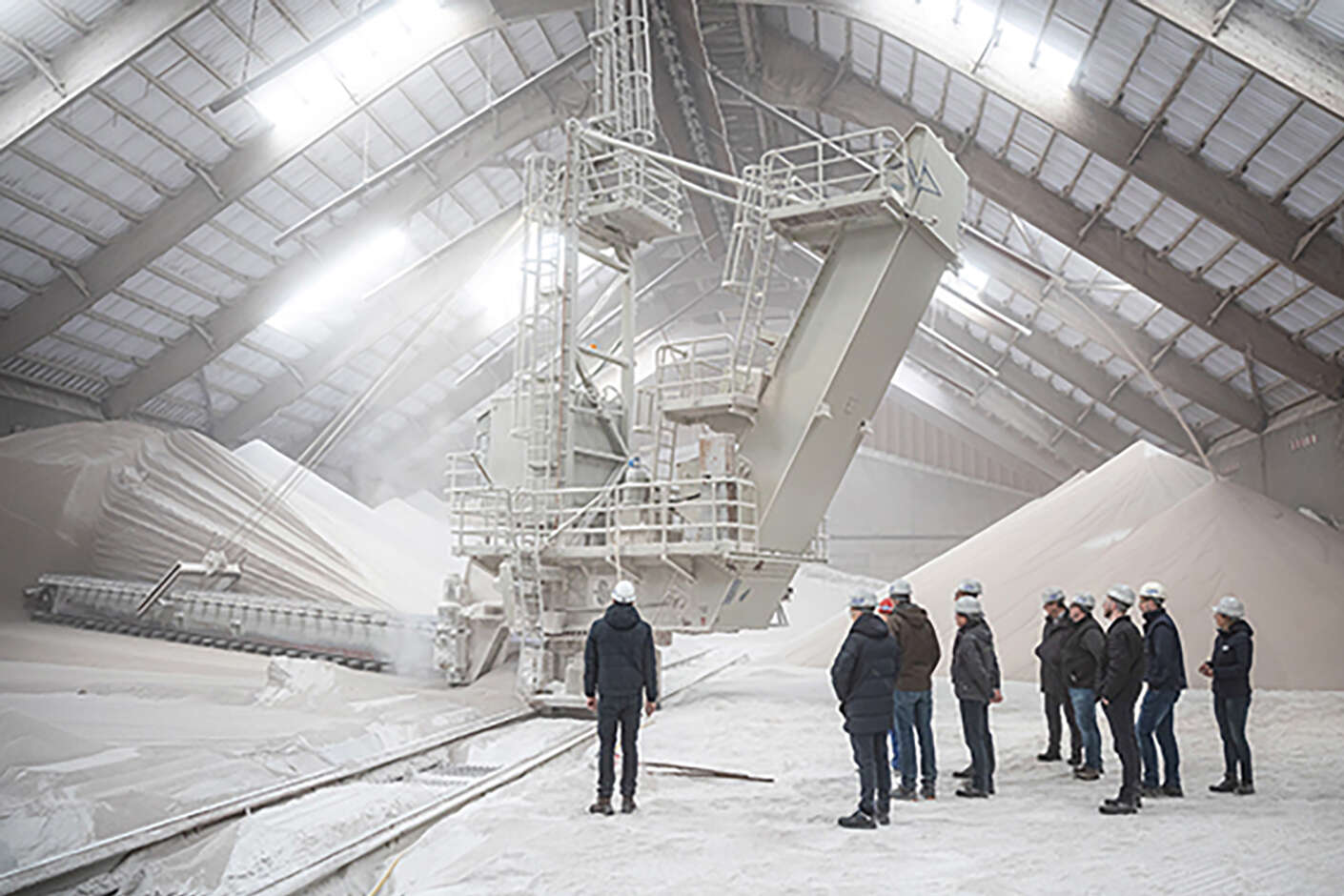 Menschengruppe steht in einer Lagerhalle mit technischen Geräten und Zucker auf dem Boden