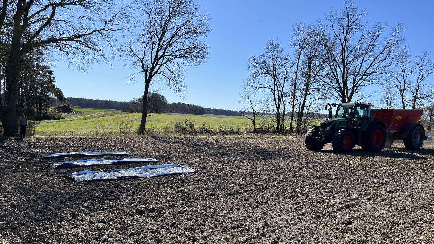 Drei weiße Planen liegen auf dem Feld, ein Traktor mit Kalkstreuer befindet sich davor