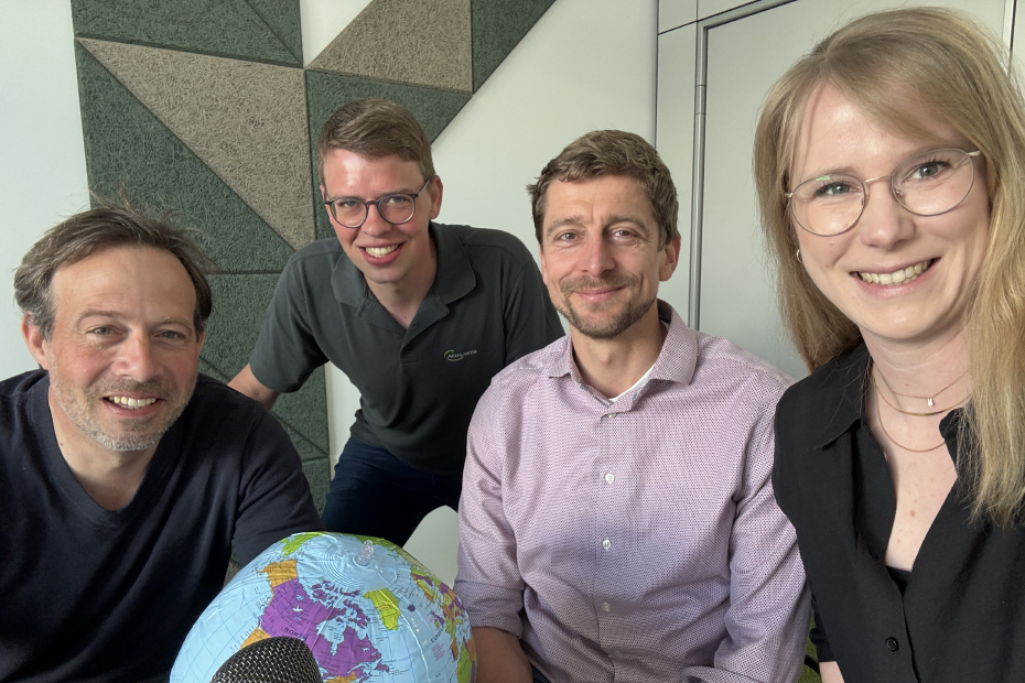 Vier Personen nehmen eine Podcastfolge auf und blicken in die Kamera.