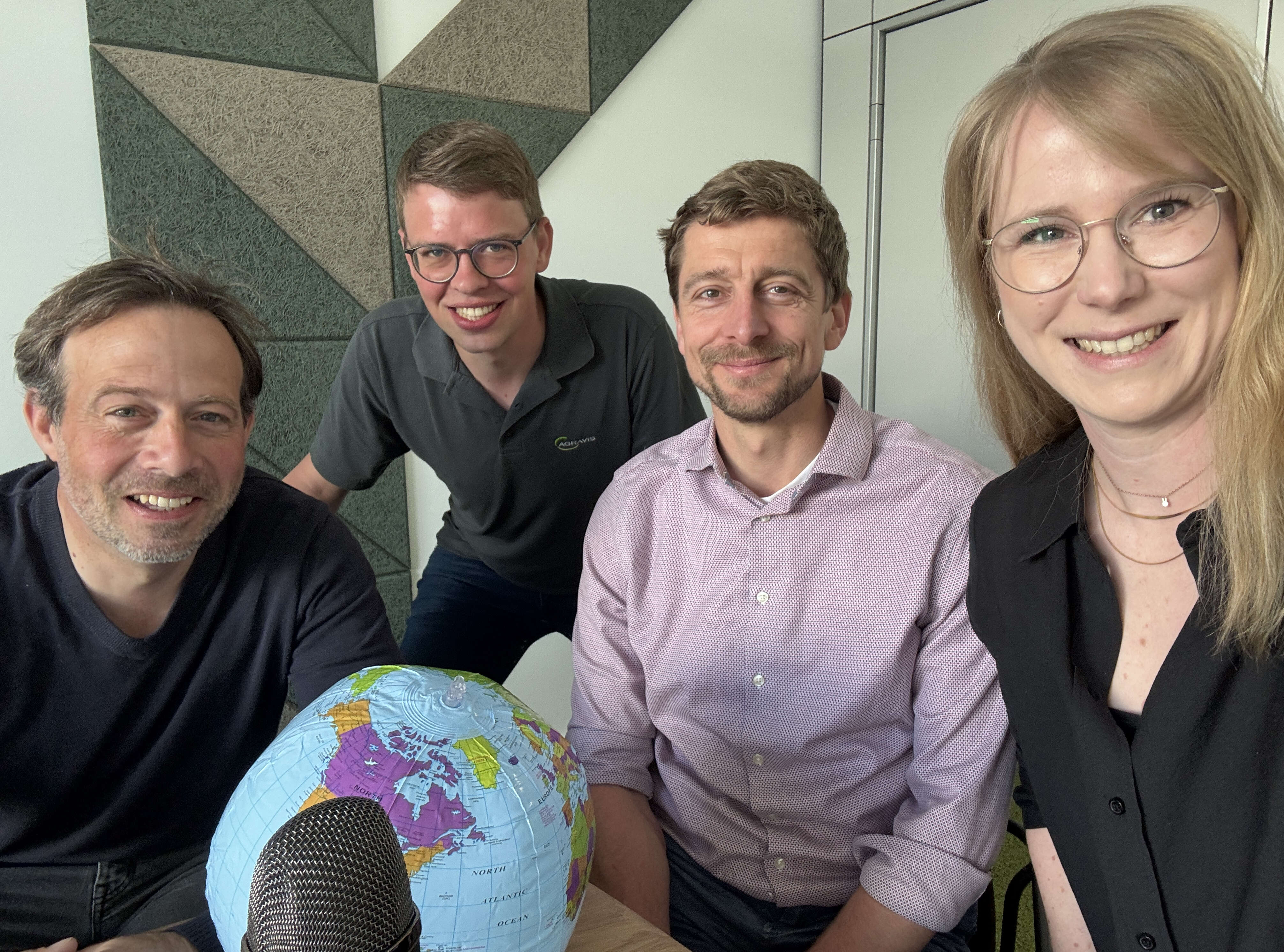 Vier Personen nehmen eine Podcastfolge auf und blicken in die Kamera.