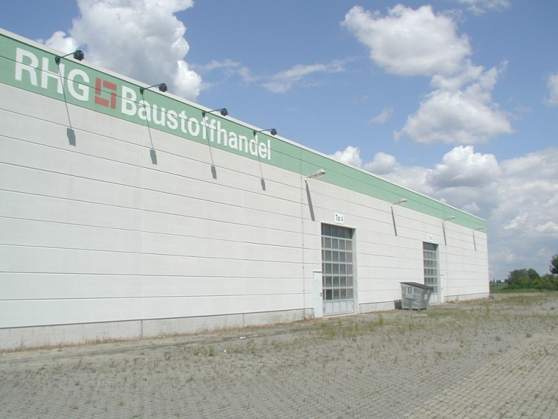 Hallenbau mit großem Tor und befestigter Freifläche bei leicht bewölktem Himmel.