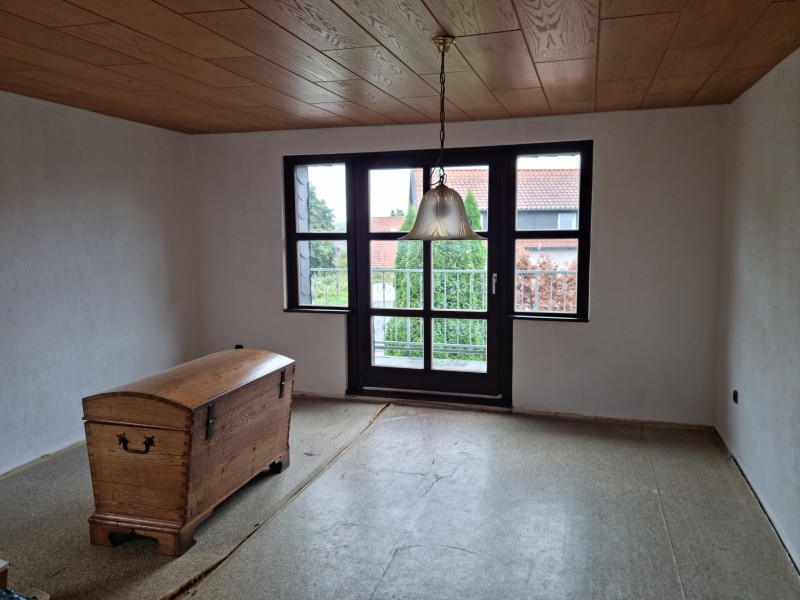 Heller Raum mit Holzdecke, großem Fenster und nostalgischer Holztruhe.