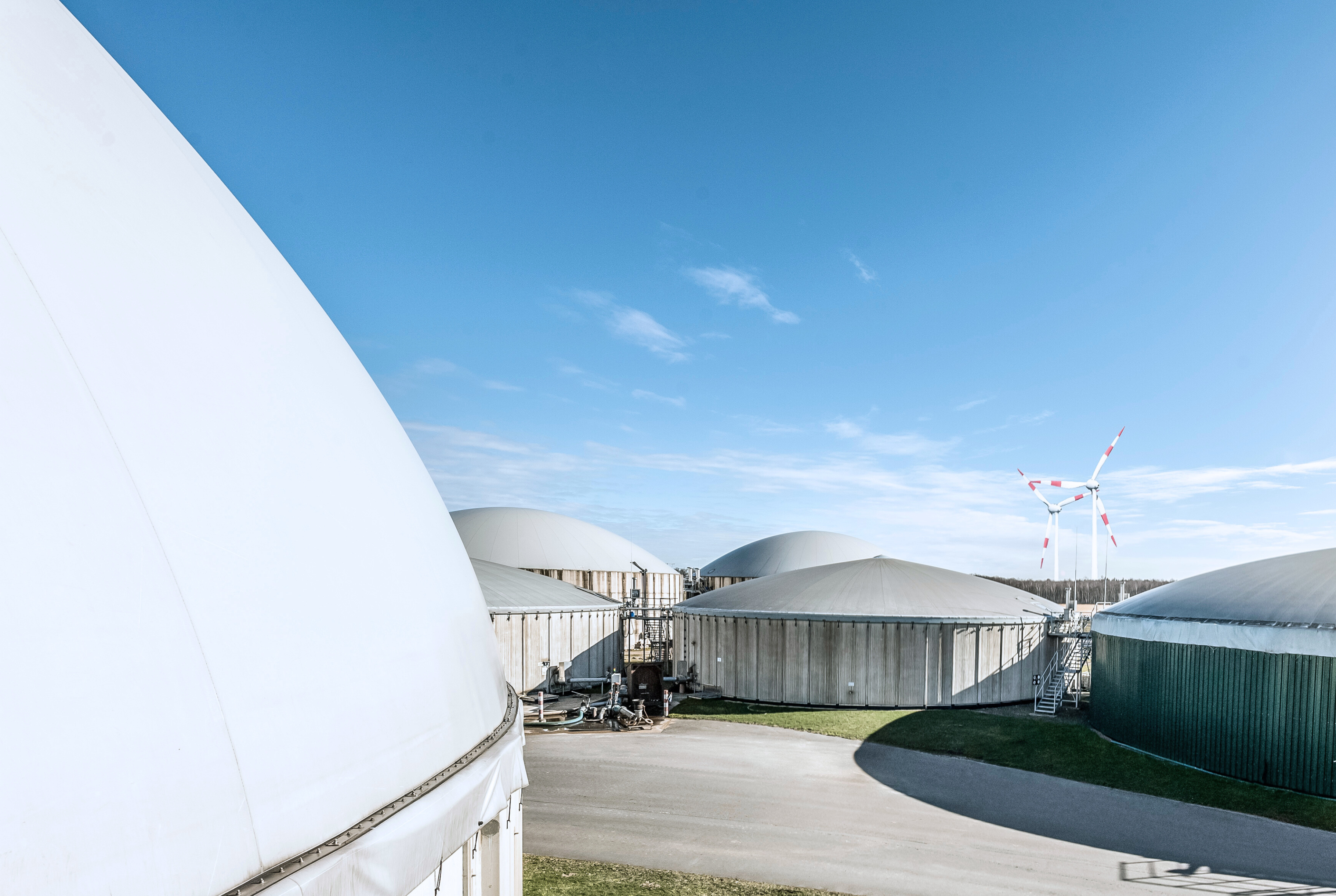 Eine Biogasanlage vor blauem Himmel. Im Vordergrund eine Gasleitung.