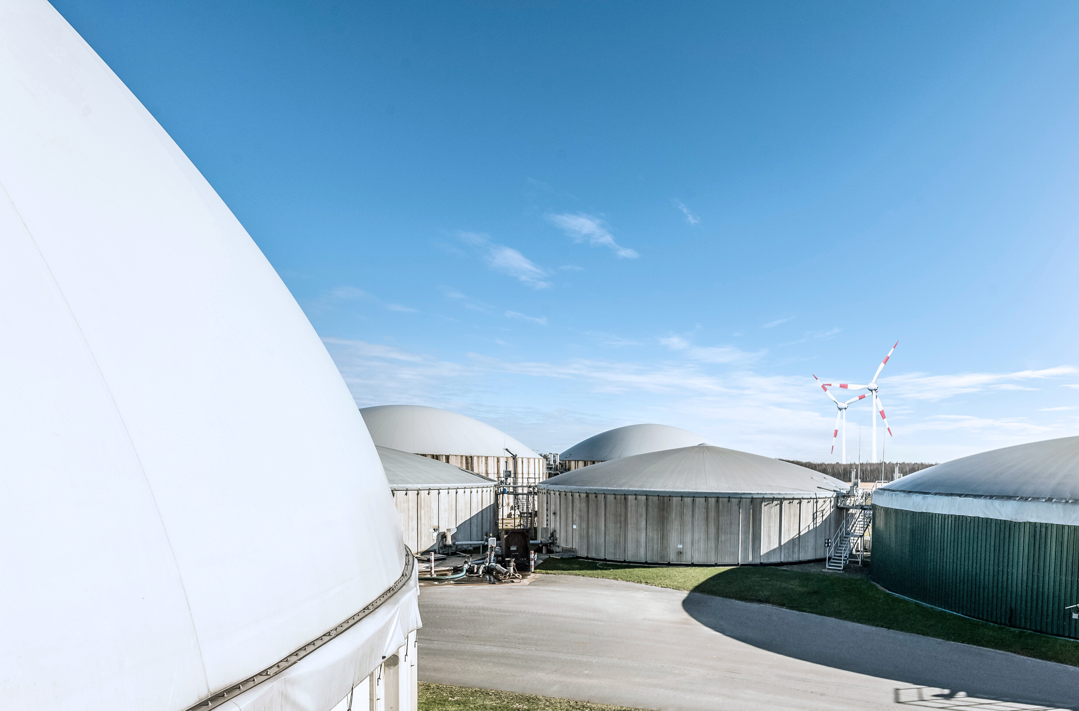 Eine Biogasanlage vor blauem Himmel. Im Vordergrund eine Gasleitung.