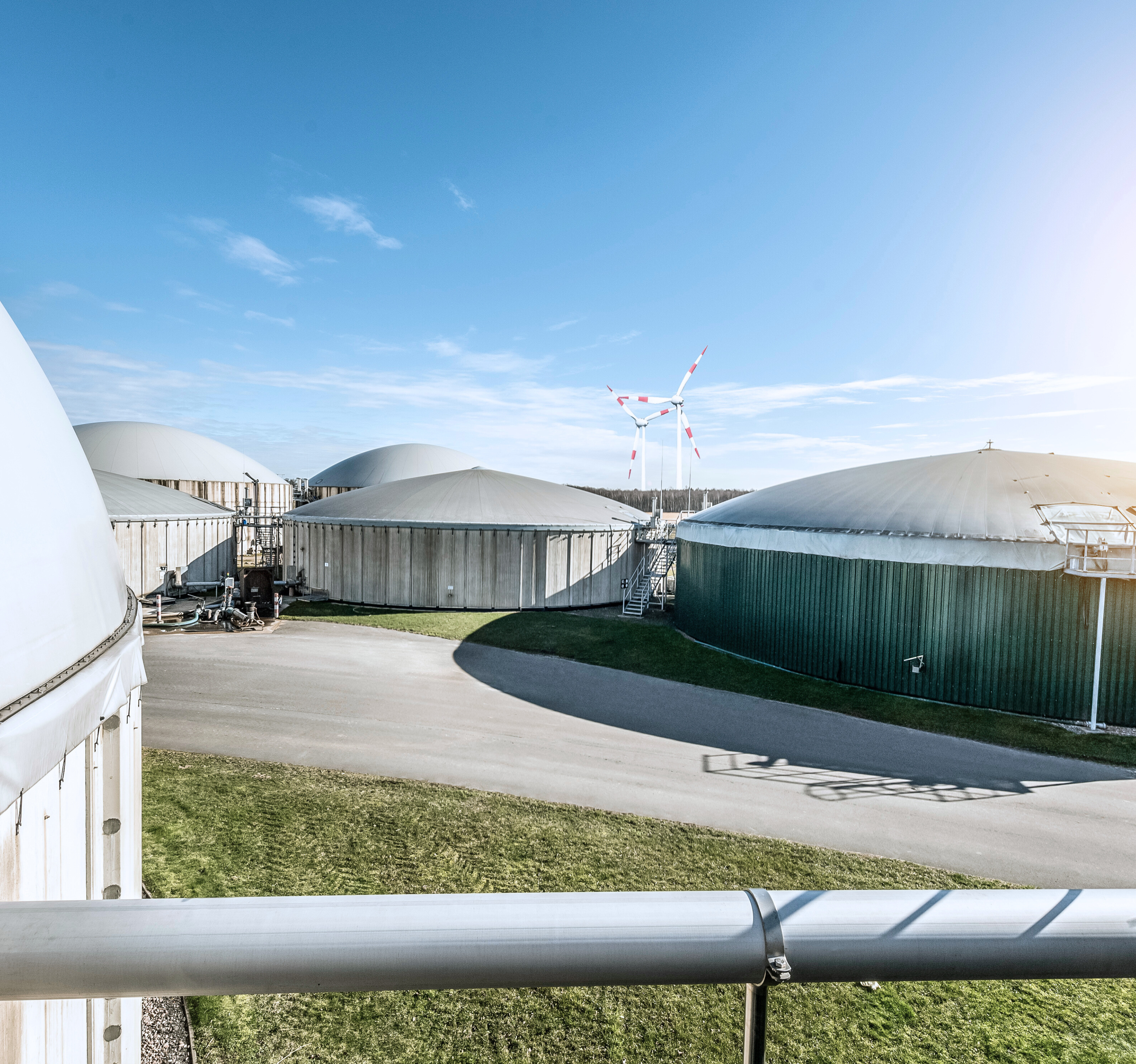 Eine Biogasanlage vor blauem Himmel. Im Vordergrund eine Gasleitung.