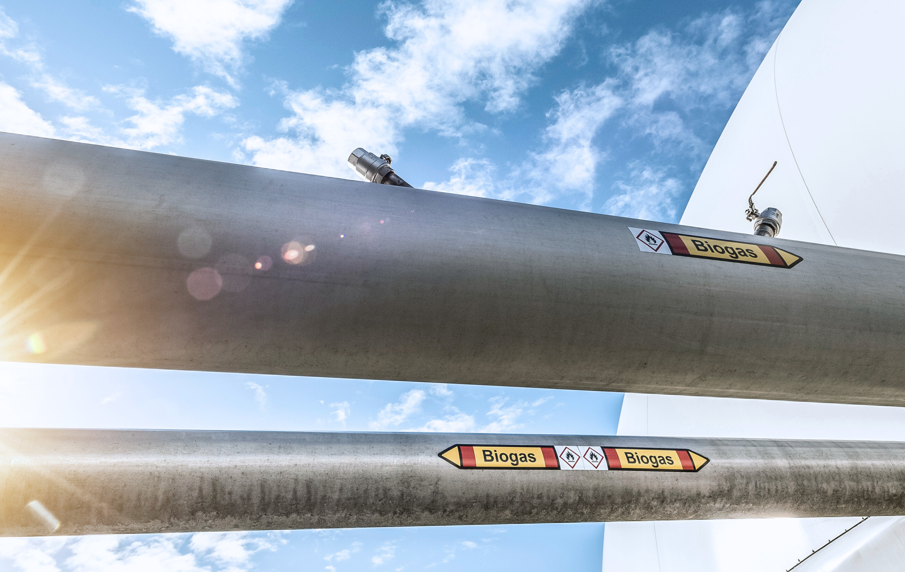Gas transportierende Leitung einer Biogasanlage. Im Hintergrund blauer Himmel mit leichten Wolken.