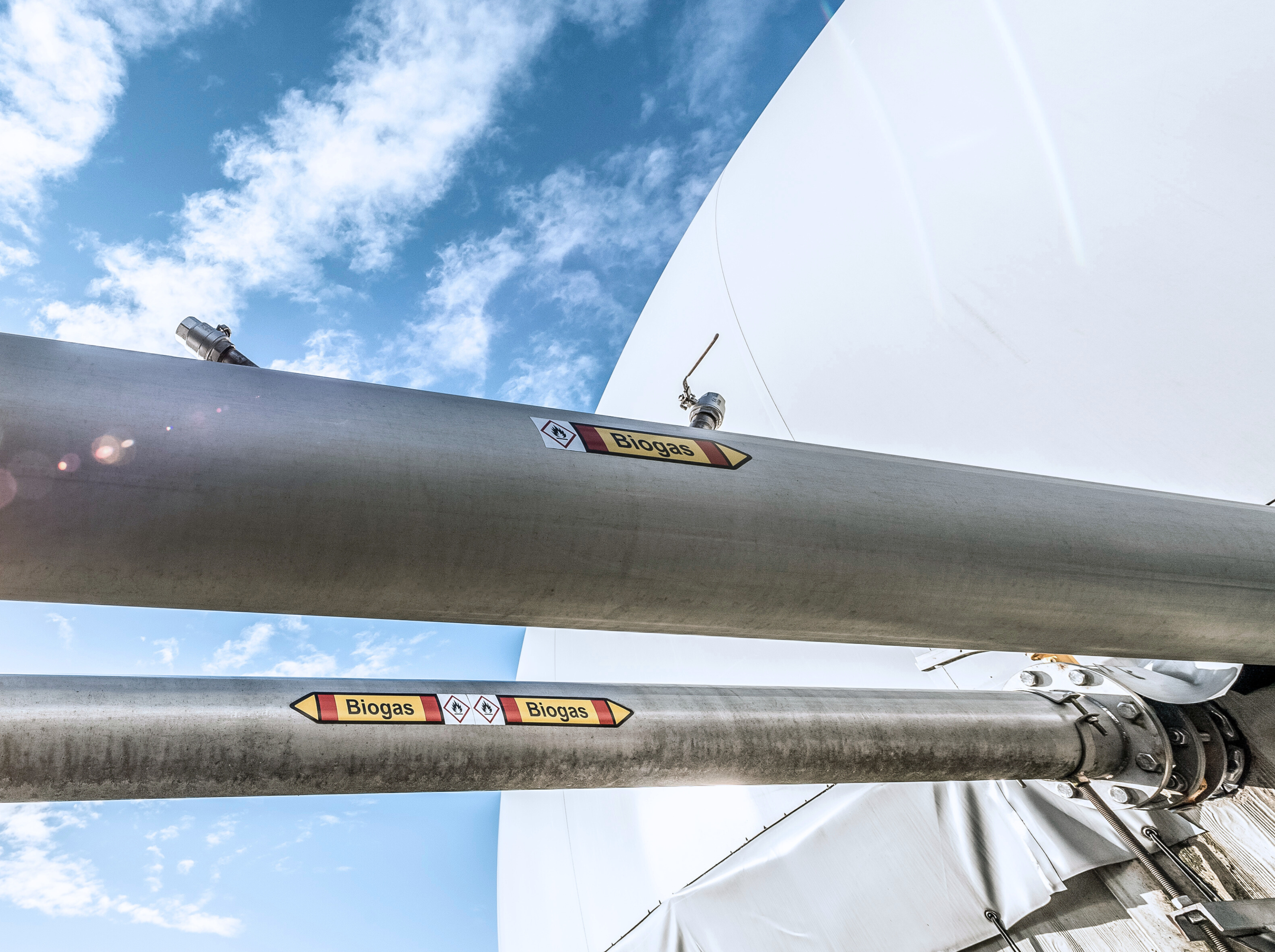 Gas transportierende Leitung einer Biogasanlage. Im Hintergrund blauer Himmel mit leichten Wolken.