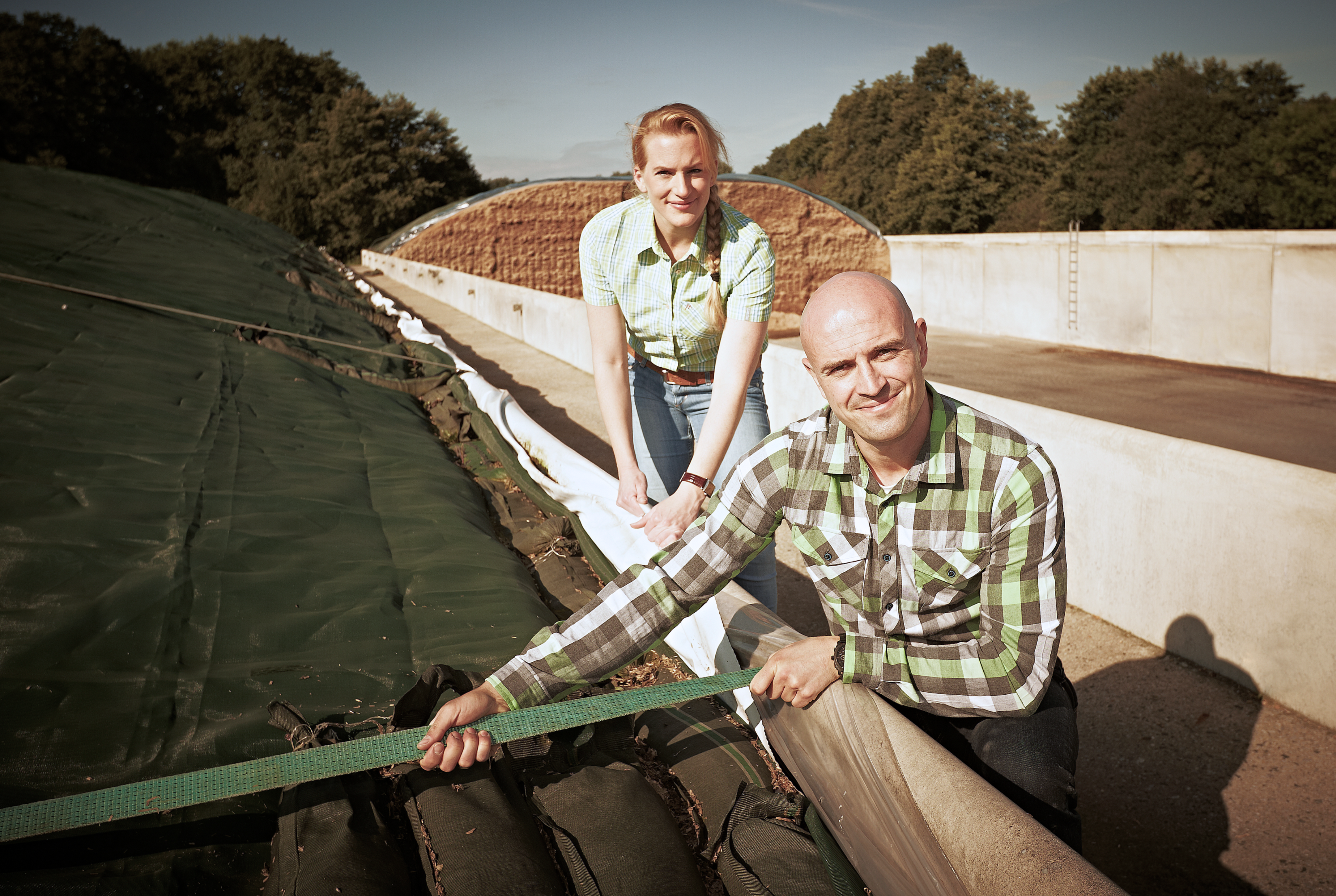Ein Mann und eine Frau knien an einem flachen Silo und halten eine Bespannung.