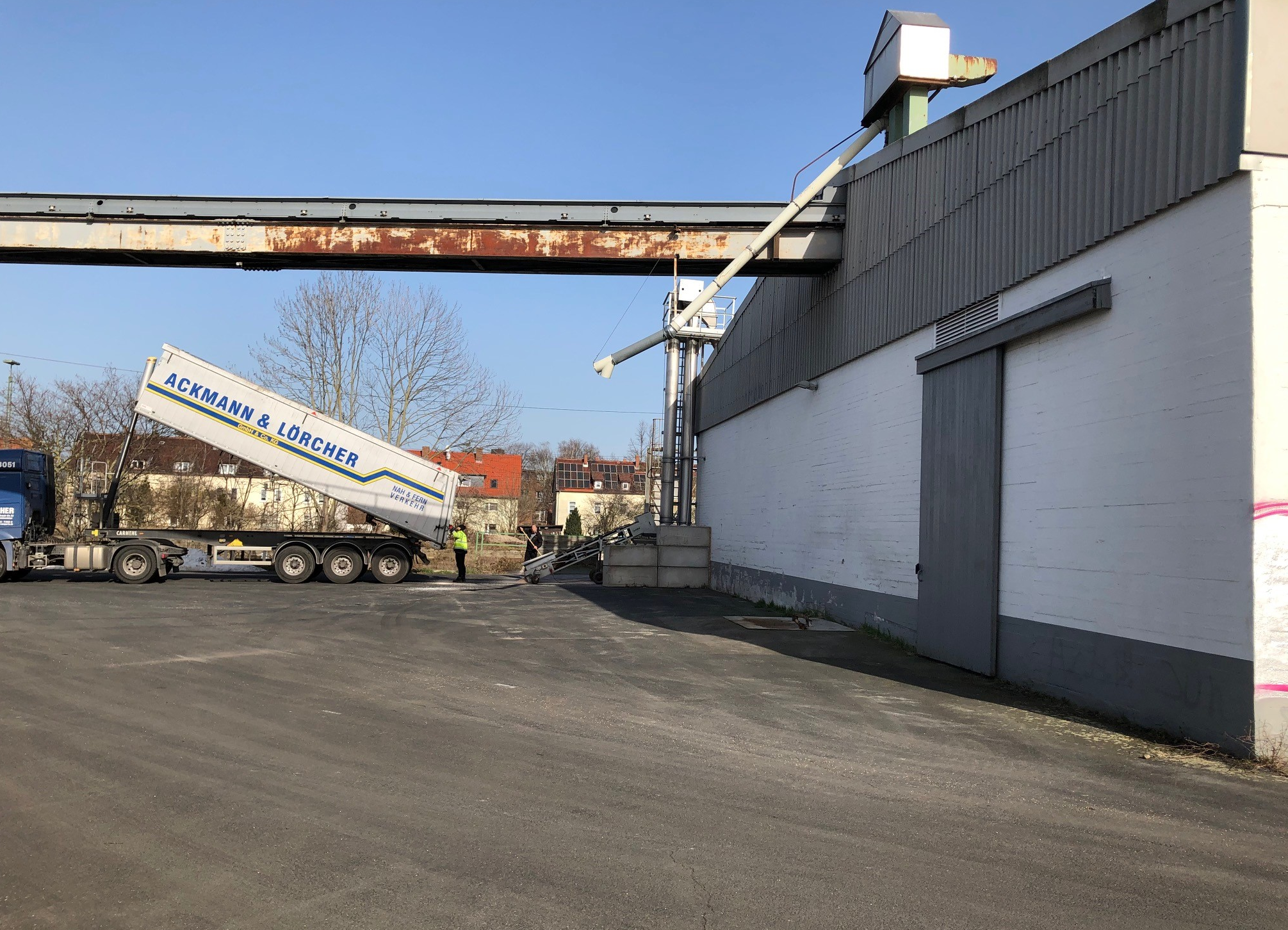 LKW beim Entladen an einer industriellen Förderanlage neben einer Lagerhalle