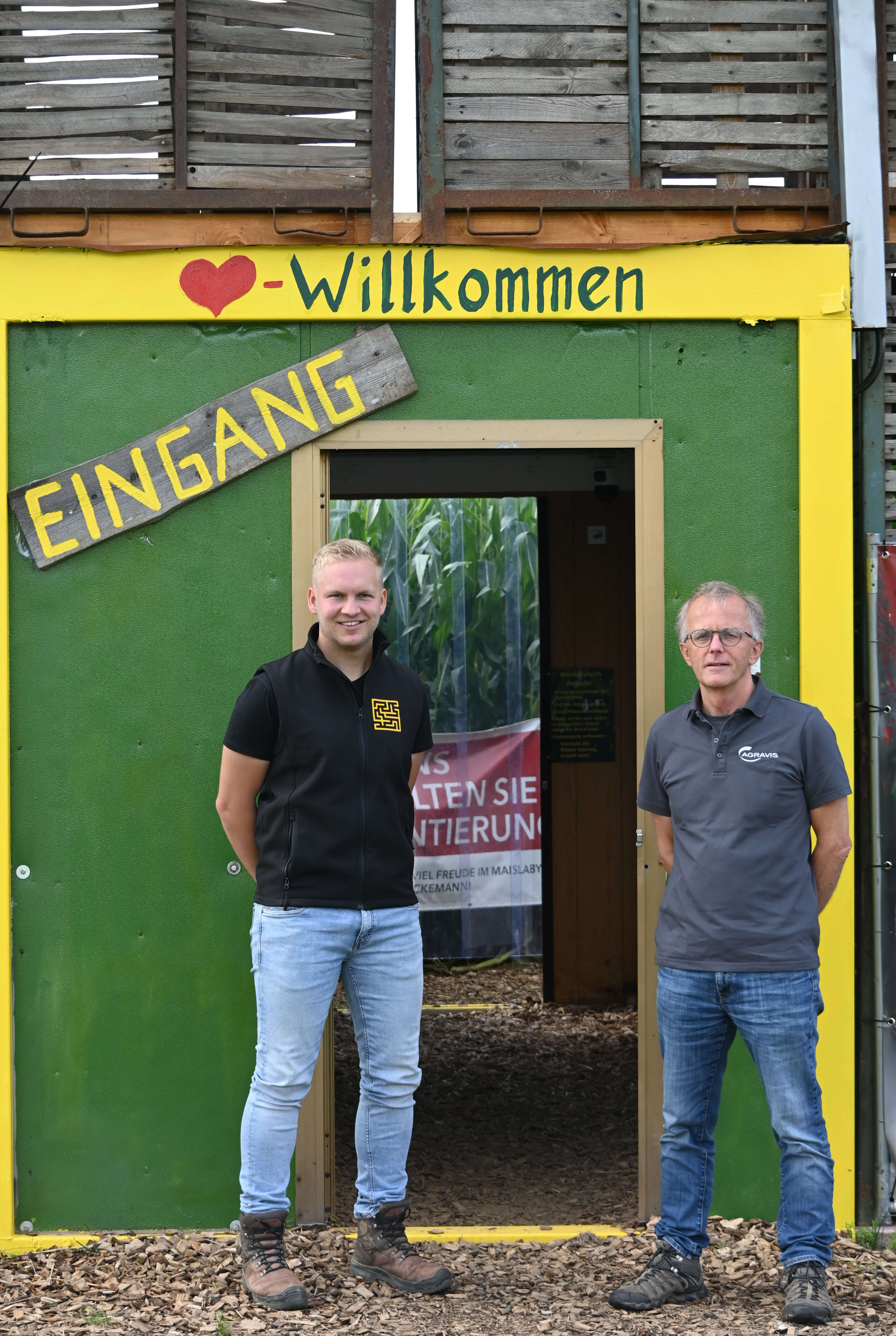 Zwei Personen stehen vor dem Eingang eines Maislabyrinths.
