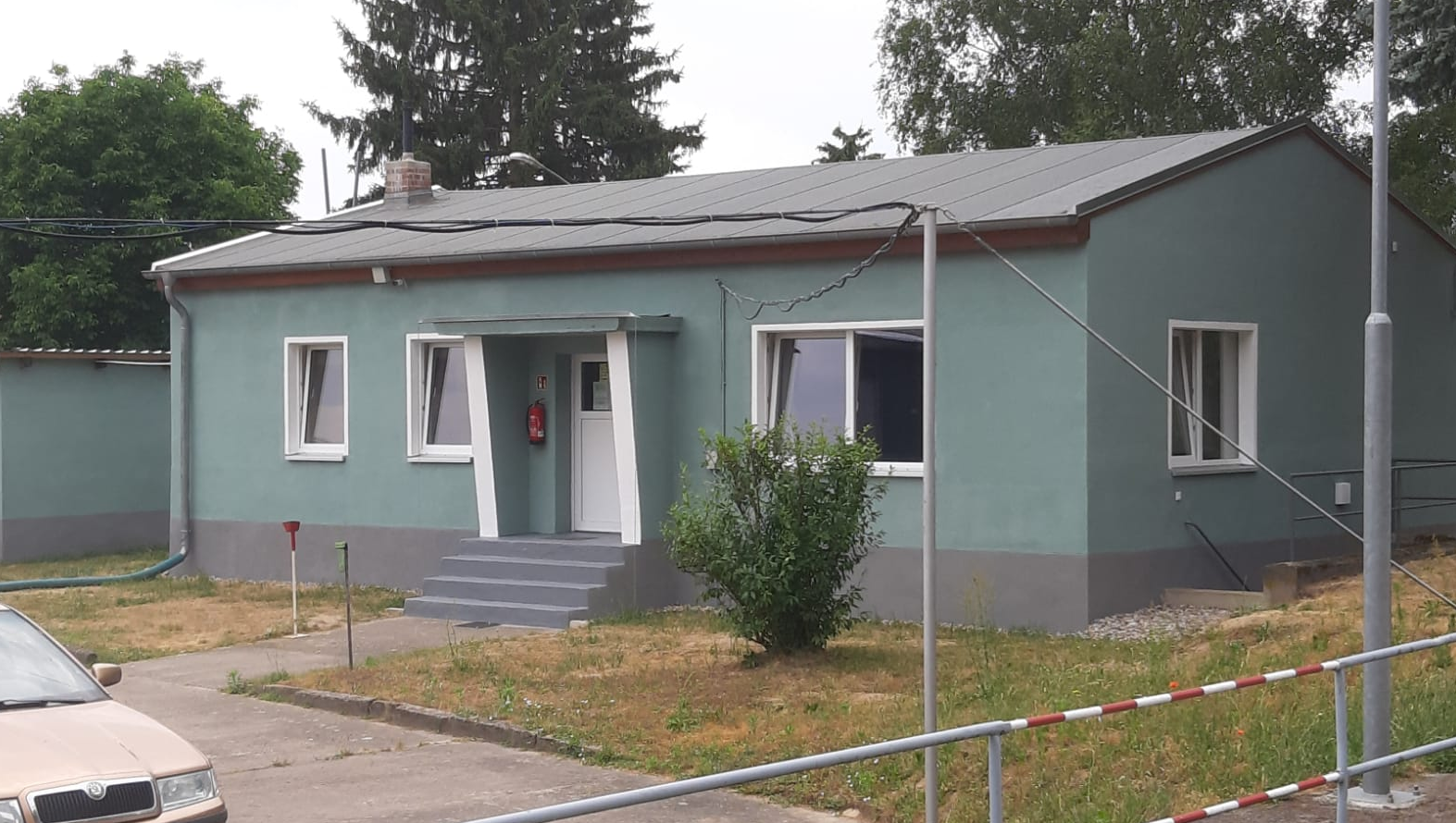 Kleines grünes Gebäude mit Flachdach und zentralem Eingang.