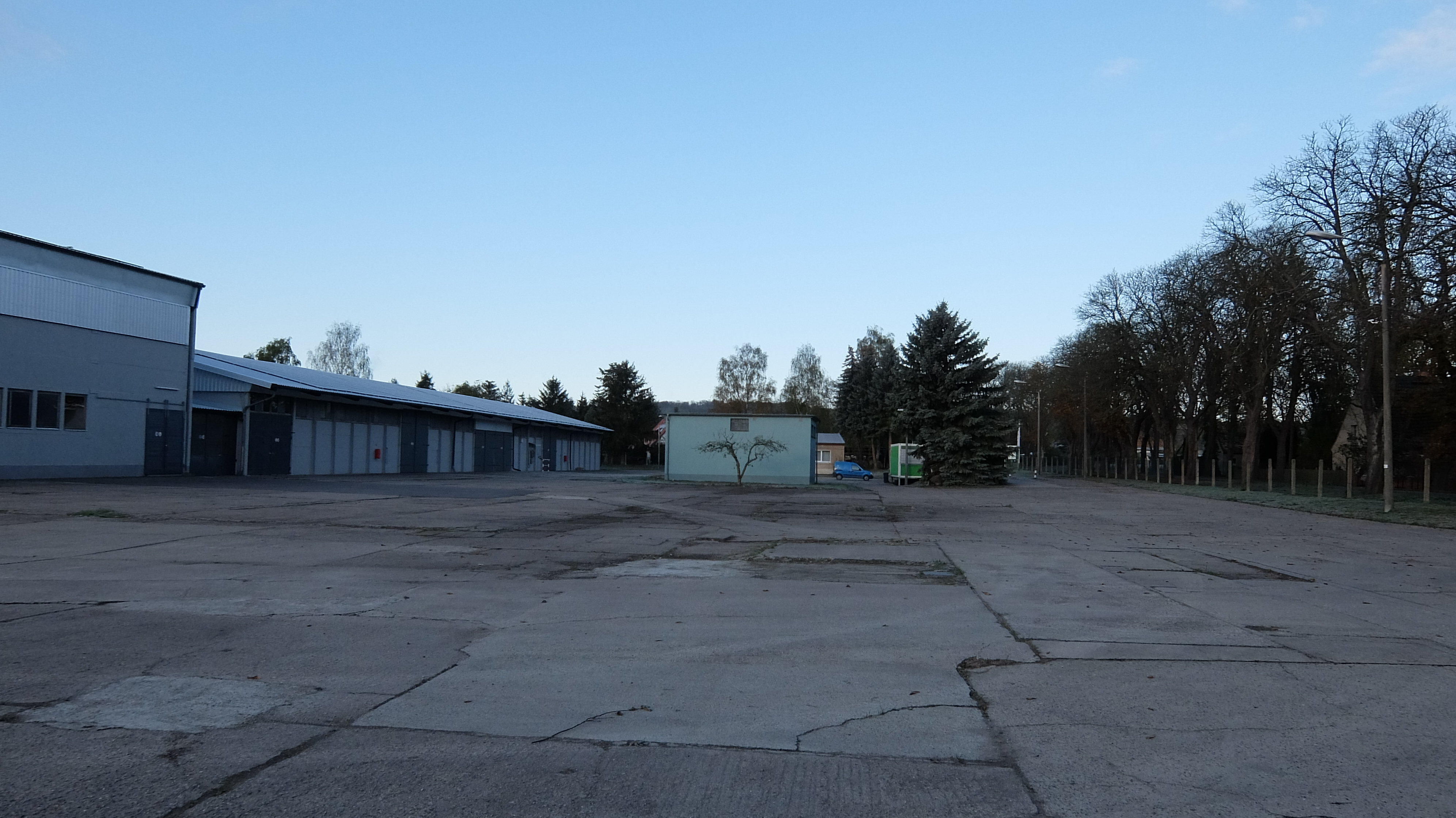 Große Asphaltfläche mit angrenzender Halle und Bäumen im Hintergrund.