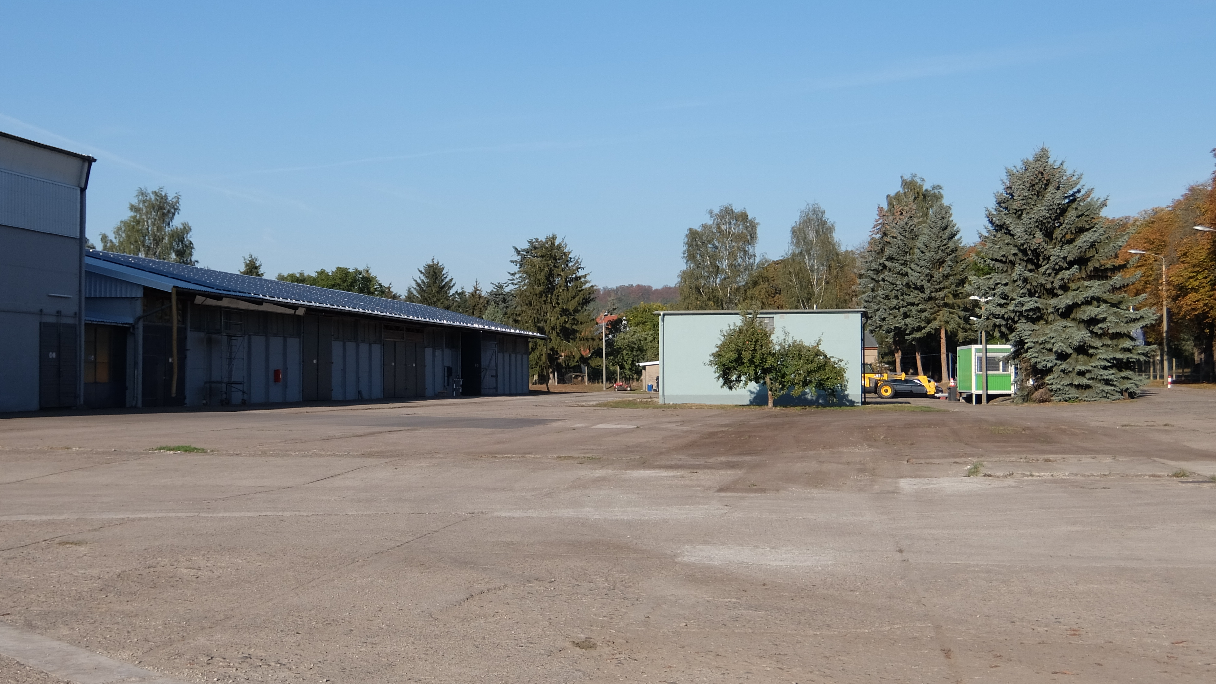 Große Asphaltfläche mit angrenzender Halle und Bäumen im Hintergrund.