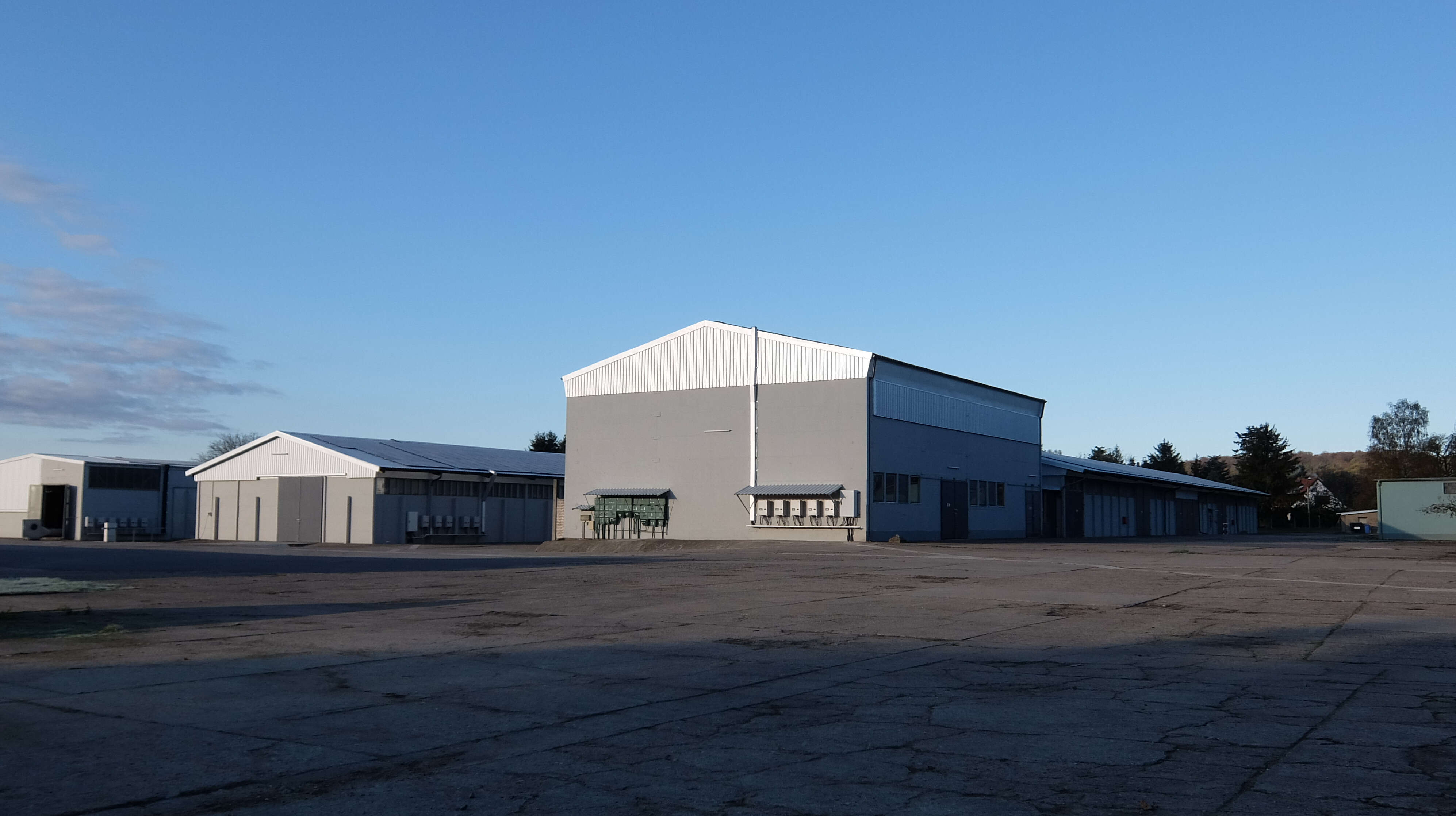 Große graue Industriehalle mit Nebengebäuden und breiter Asphaltfläche.